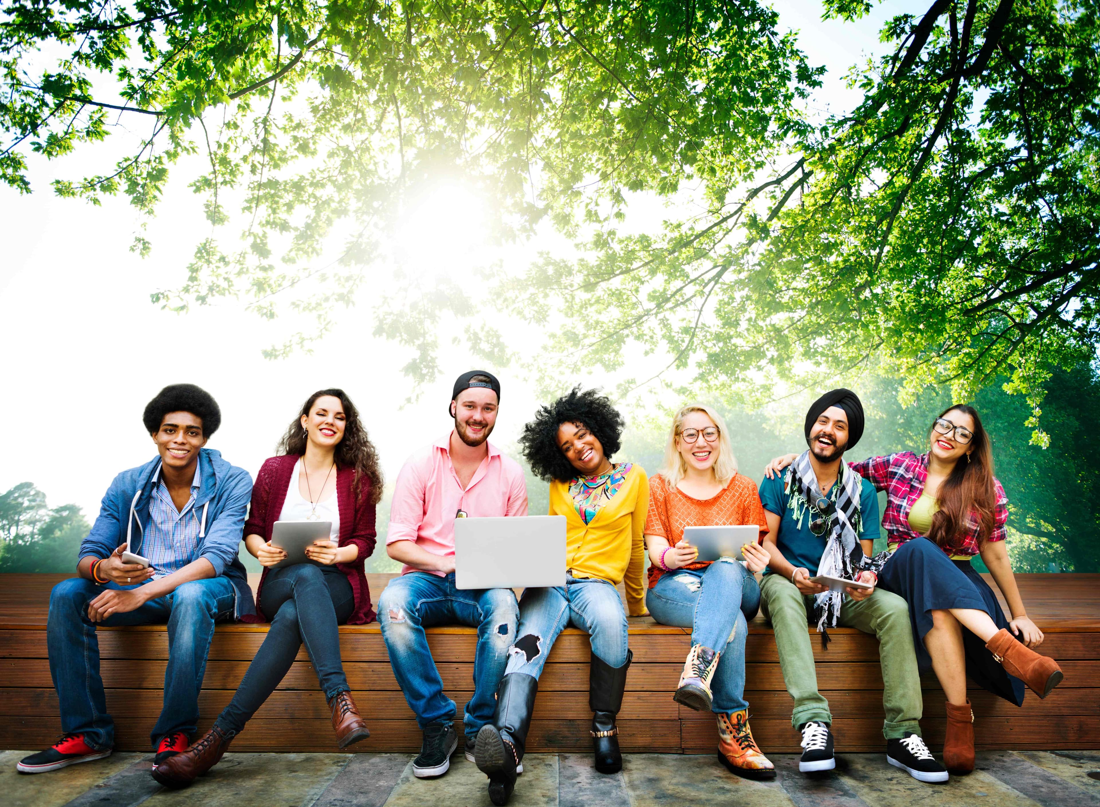 Diverse group of international students sitting outdoors with laptops and tablets