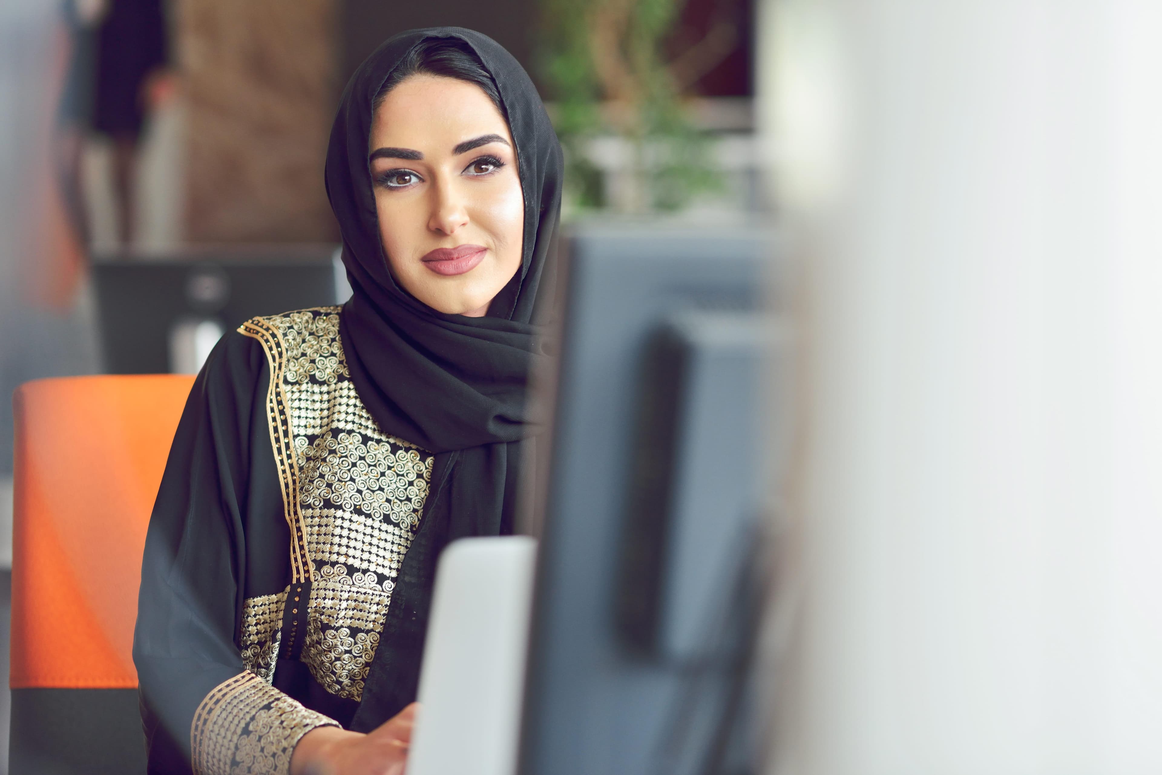 A focused woman in traditional attire studying at a computer in a modern office